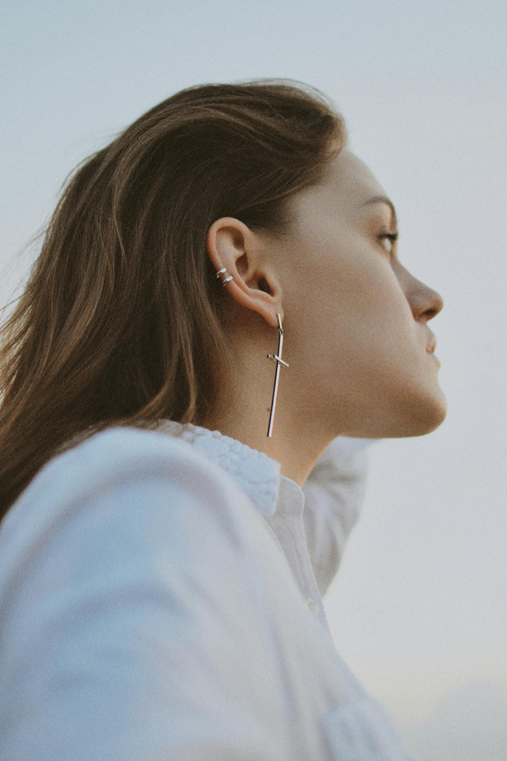 A serene side profile portrait of a woman wearing a stylish dangle earring against a bright sky.